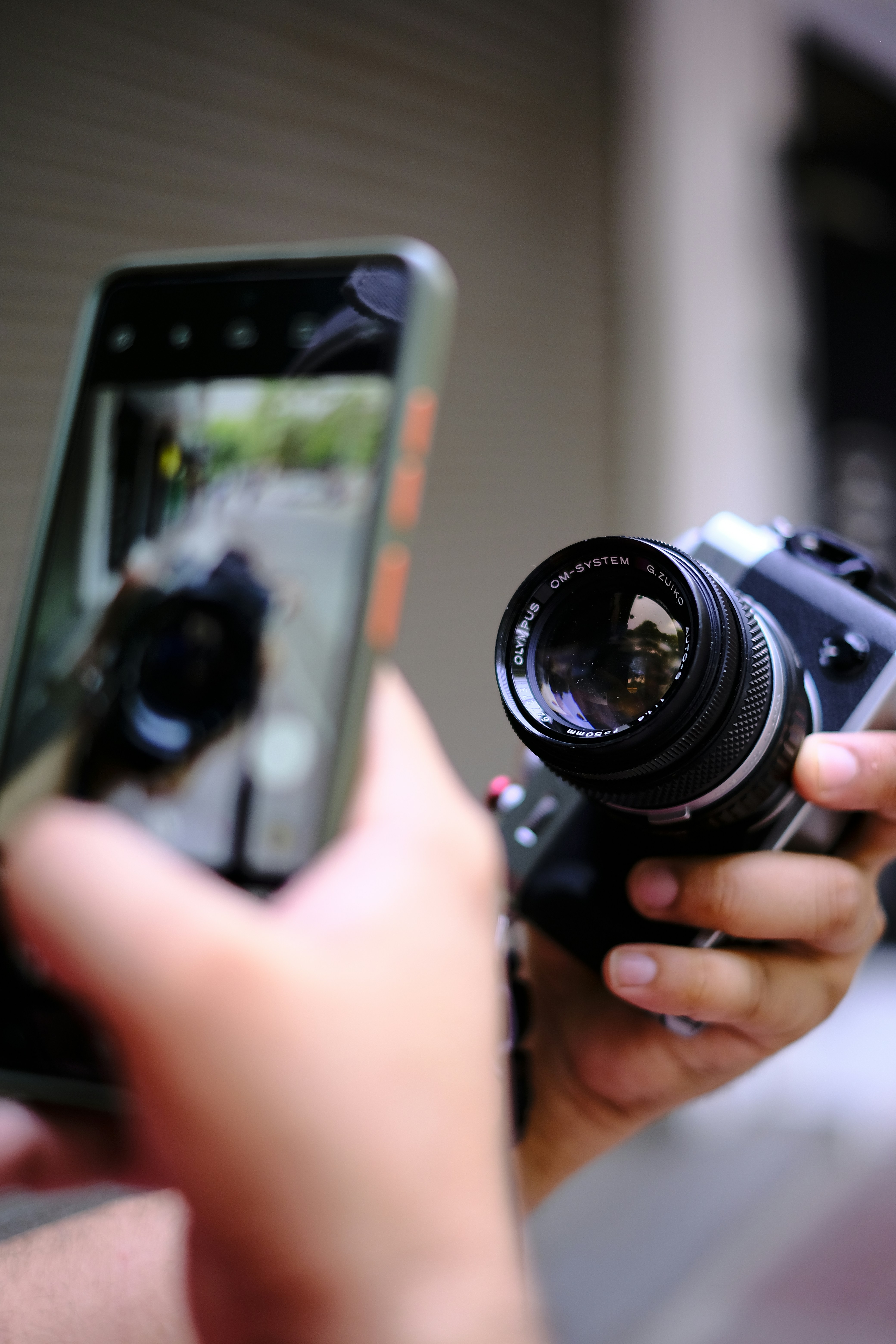 Hand holding a smartphone alongside a DSLR camera with telephoto lens